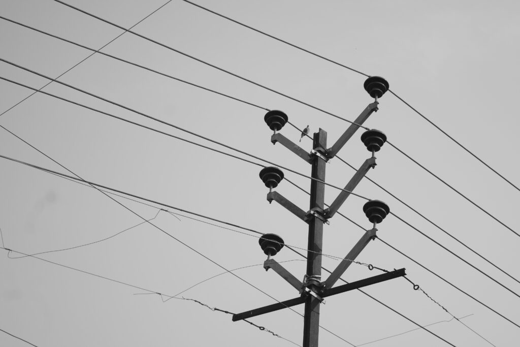 A low angle monochrome photo of a utility pole with power lines against the sky.